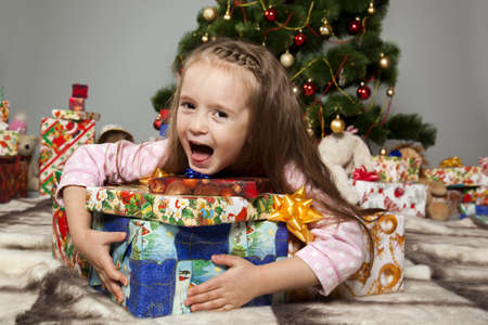 Girl in pajamas lying under the Christmas tree with gift in handの写真素材