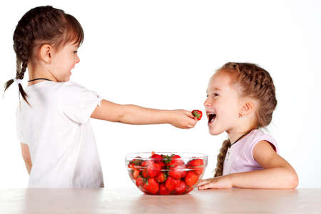 Two little girls feed each other strawberries with a full bowl of strawberriesの写真素材