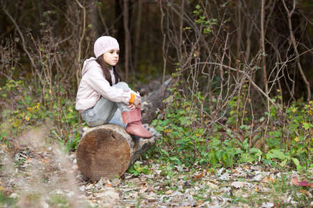beautiful girl sitting on a log in the autumn forestの写真素材