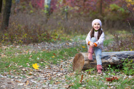 beautiful girl sitting on a log in the autumn forestの写真素材