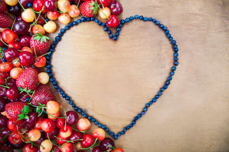Many fresh fruit lying around the heart of blueberries on a wooden boards backgroundの写真素材