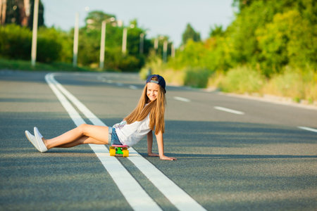 A young girl with penny board outside the city at the road.