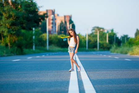 A young girl with penny board outside the city at the road.の写真素材
