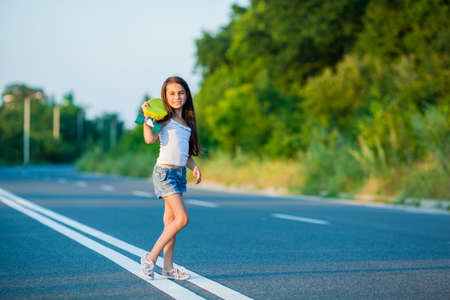 A young girl with penny board outside the city at the road.の写真素材