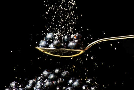 Spoon with huckleberry with pouring sugar on black backgroundの写真素材