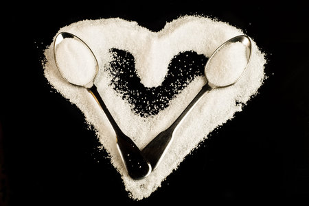 Heart-shaped sugar pile and metal spoons isolated on black backgroundの写真素材