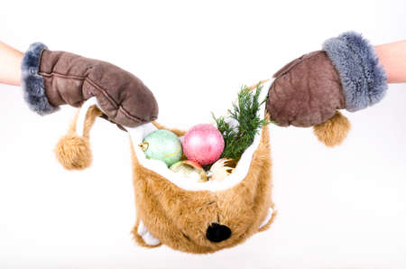 Bear hat filled with Christmas decorations holds by hands with fur mittenの写真素材