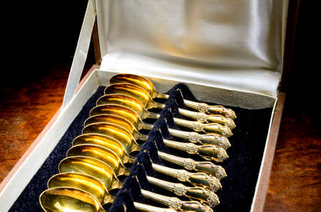 Box of vintage gold-plated teaspoons on mahogany tableの写真素材