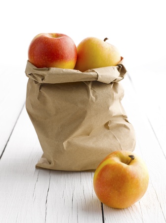 Apples in paper bag on white wooden tableの写真素材
