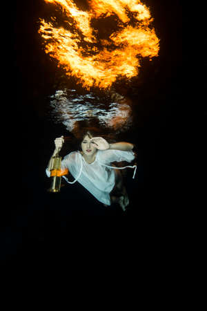White dressed woman dives underwater with a laternの写真素材