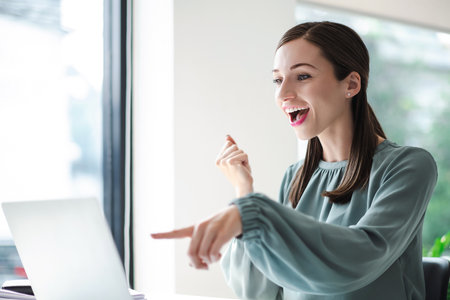 Beautiful businesswoman celebrate with laptop success happy pose. E-commerce, university education, internet technology, or startup small business concept. Modern office.の写真素材
