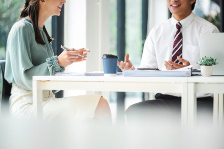 Young confident business people sitting at the office table working on laptop computer with partner,...
