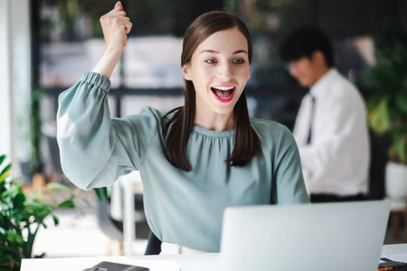 Beautiful businesswoman celebrate with laptop success happy pose. E-commerce, university education, internet technology, or startup small business concept. Modern office.の写真素材
