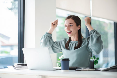 Beautiful businesswoman celebrate with laptop success happy pose. E-commerce, university education, internet technology, or startup small business concept. Modern office.の写真素材