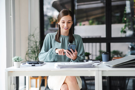 Young confident businesswoman sitting at the office table working on laptop computer and smart phone mobile.の写真素材