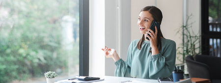 Young confident businesswoman sitting at the office table working on laptop computer and smart phone mobile. For banner design.の写真素材