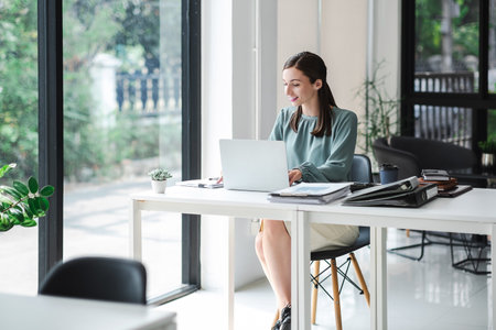Young confident businesswoman sitting at the office table working on laptop computer.の写真素材