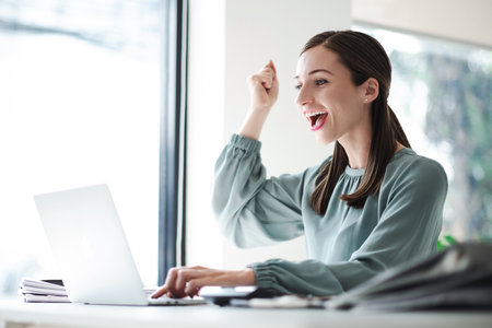 Beautiful businesswoman celebrate with laptop success happy pose. E-commerce, university education, internet technology, or startup small business concept. Modern office.の写真素材