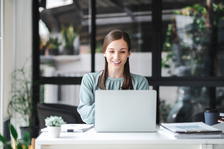 Young confident businesswoman sitting at the office table working on laptop computer. Business concept.の写真素材