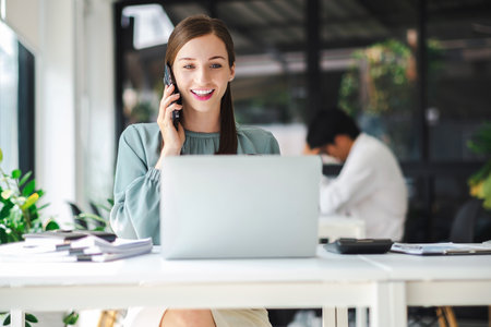 Young confident businesswoman sitting at the office table working on laptop computer and smart phone mobile.の写真素材