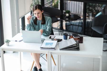 Young confident businesswoman sitting at the office table focused working on laptop computer. Business concept.の写真素材