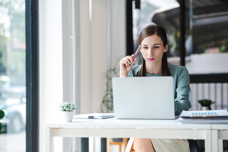 Young confident businesswoman sitting at the office table focused working on laptop computer. Business concept.の写真素材