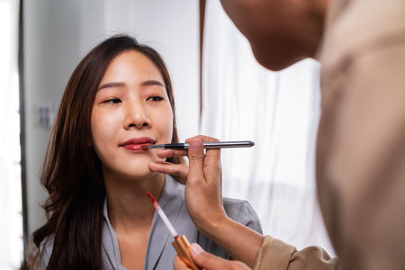 Hand of make up artist painting lips of young beauty model asian girl . Make up in process.の写真素材