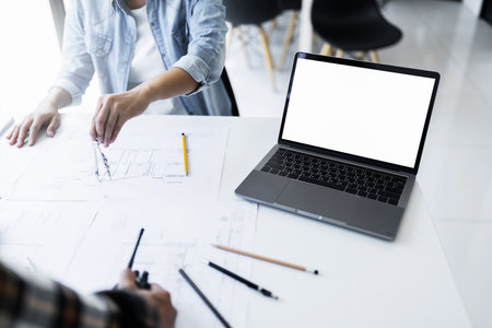 Image of laptop empty white screen and engineer meeting for architectural project. working with partner and engineering tools on workplace mockup.の写真素材