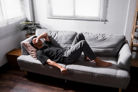 Stressed man lying on sofa holding glasses for relax.の写真素材