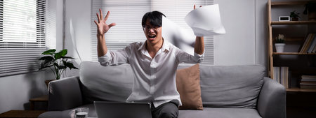Angered, furious, crazy and mad millennial Asian businessman or man office worker screaming, shouting and throwing up papers at him office desk. Depression, overworked, failure, banner design.の写真素材