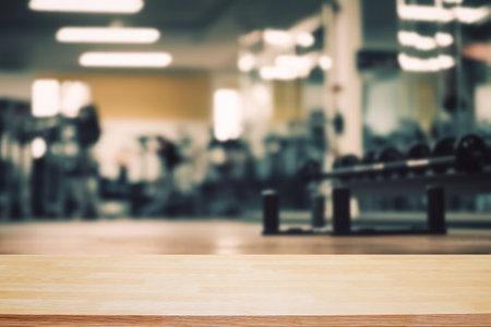 Blurred background of fitness gym and wooden table free space for product display.の写真素材