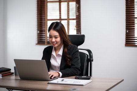 Young confident businesswoman sitting at the office table working on laptop computer. Business concept.の写真素材