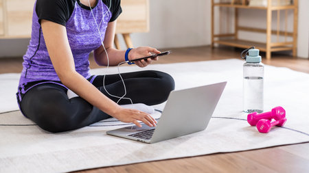 Asian woman in sports wear doing workout at home with laptop and dumbbells. home exercise conceptの写真素材
