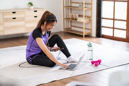 Asian woman in sports wear doing workout at home with laptop and dumbbells. home exercise conceptの写真素材