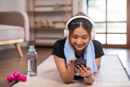 Asian woman in sports wear enjoy doing workout at home with smart phone or laptop. home exercise conceptの写真素材