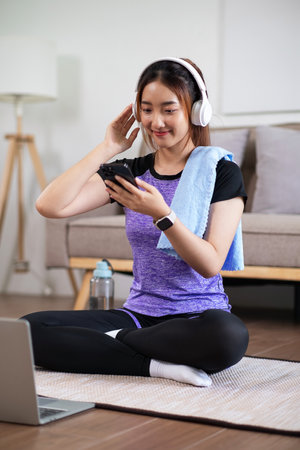 Asian woman in sports wear enjoy doing workout at home with smart phone or laptop. home exercise conceptの写真素材