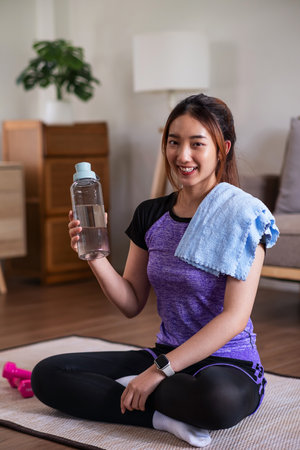 Asian woman taking break after exercise with drinking water at the home. home exercise conceptの写真素材