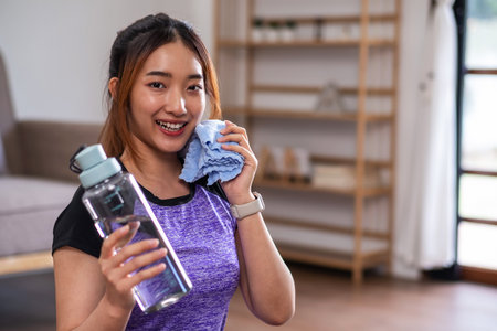 Asian woman taking break after exercise with drinking water at the home. home exercise conceptの写真素材