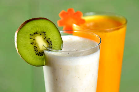 Two smoothie cocktails (fruit of kiwi and vegetable of carrot) on green backgroundの写真素材