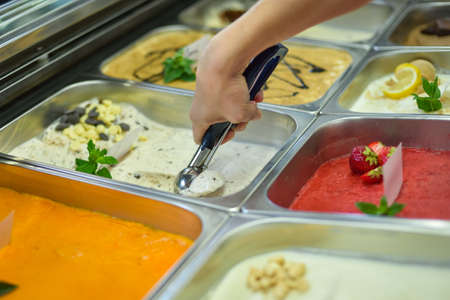 Hand with tongs (spoon) scooping a scoop of ice cream from a cooling box from a tray