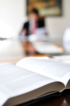 Close-up of an open book on an office desk with a blurred man in the background