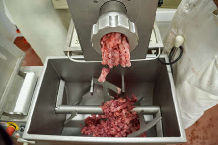 Filling comes out through raw meat grinder sieve. Grinder closeup. Electric mincer machine with fresh chopped meat. Process of meat grinding in kitchen with mincing machine. Preparation of minced beefの写真素材