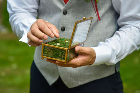 Wedding engagement rings close up lying on moss in a box in the hands of the groom. Nature wedding. Rustic style decoration. Selective focus.の写真素材