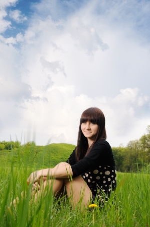 Girl sitting on green grass with blue sky and cloudsの写真素材