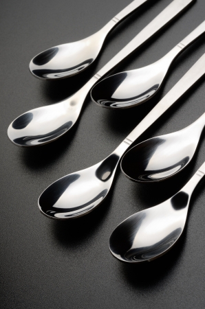 Teaspoons lined in a row on a black grained surfaceの写真素材