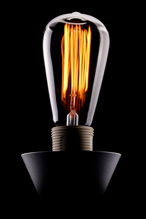 A classic Edison light bulb glowing on black backgroundの写真素材