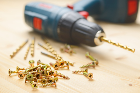 Heap of metal screws and electric drill in wooden boardの写真素材