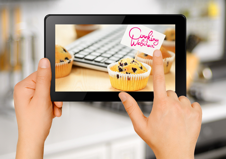Hands holding black tablet computer with muffins on the screen. Cooking webinar conceptの写真素材