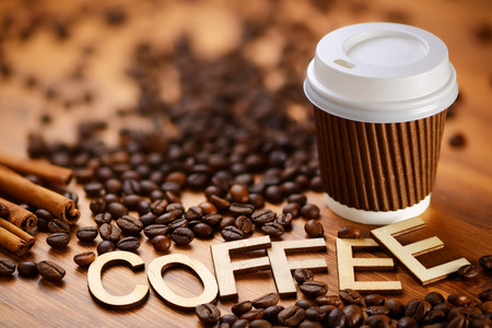 Paper cup and Coffee word written with wooden letters on beans heap. Beverage to go conceptの写真素材