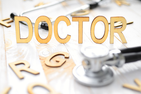 Word doctor made with wooden letters and stethoscope on the white plank tableの写真素材
